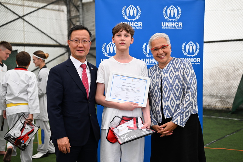 UNHCR Representative and ROK Ambassador posing with a Ukrainian boy holding a certificate