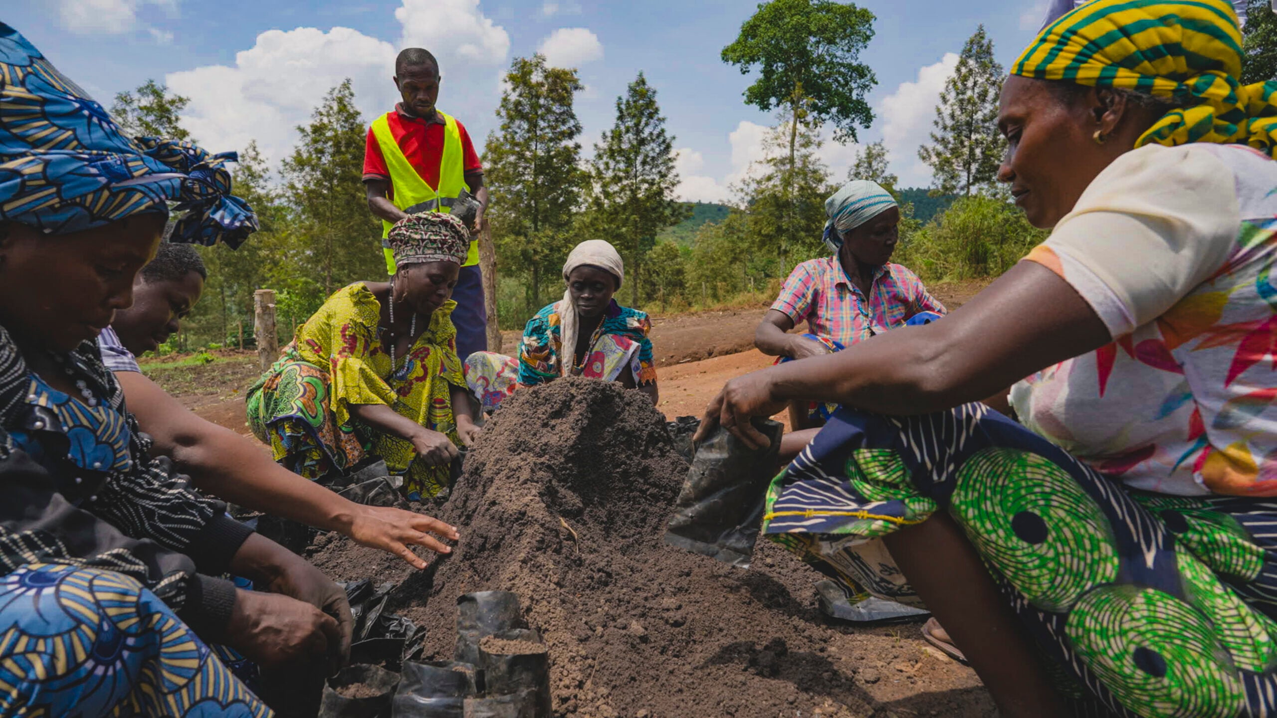 A group of women is packing soil into small black plastic bags. 