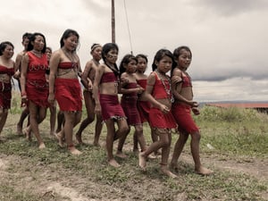 A group of young indigenous people wearing traditional dress walk together near their village