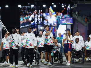 Un groupe d'athlètes, certains marchant et d'autres se déplaçant en fauteuil roulant, défile devant un écran géant.