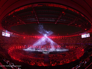 Des faisceaux de lumière blanche forment un cône géant au centre d'un stade plongé dans l'obscurité, dans le cadre d'un spectacle de lumière.