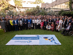 A large group of people pose for a group photo on a lawn with a banner in front.