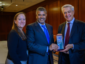 A woman and two men pose for the picture, holding a small glass certificate with the UNHCR logo.
