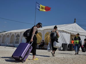 People carrying bags and pulling suitcases walk towards a large tent with a Moldovan flag flying above it