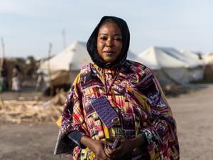 A woman in a colourful dress stands in front of rows of white tents in an IDP camp.