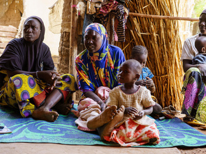 Mali. Newly arrived Burkinabe women and children sitting on a plastic mat lent by a member of the host community
