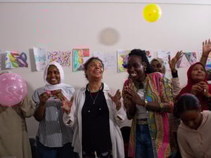 Women clap and smile and throw balloons in the air.