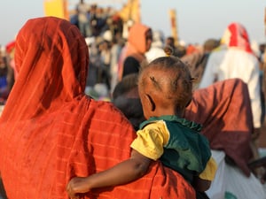 Une femme en orange est photographiée de dos, portant son enfant.