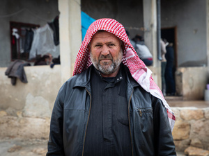 Un homme portant un foulard rouge et une veste en cuir se tient devant un bâtiment.