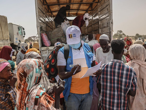 A UNHCR staff member checks documents in a group of people standing at the back of an open truck.