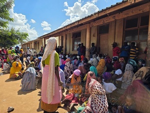 Large groups of people gather, waiting to receive assistance outside a school. 