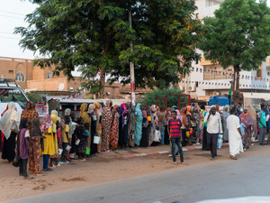 Families from El Fasher queue outside along a street.