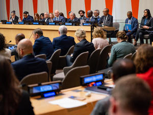 Delegates and officials attend a meeting at UN Headquarters, with speakers seated on a panel before an audience.