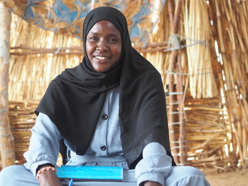 Fathia, a Sudanese refugee lawyer, holds documents and smiles at the camera.