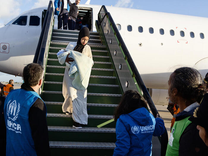 A Somali woman holding a baby is greeted by UNHCR staff as she exits a plane after being evacuated from Libya to Italy. 