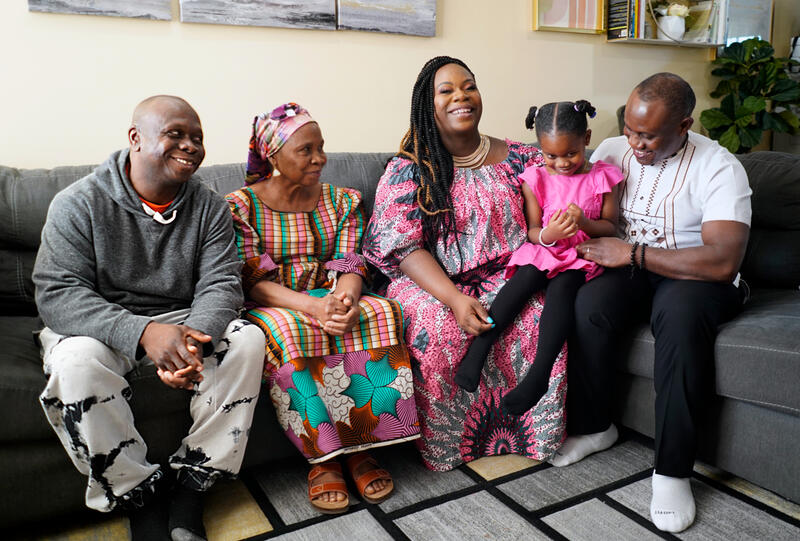 Four adults and a young girls sit on a couch together.
