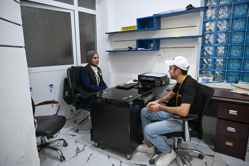 A UNHCR staff member assists a man as he disembarks from a boat in a harbour.