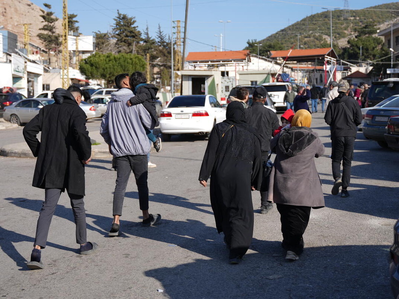 Groups of people pictured walking, from behind, next to parked cars