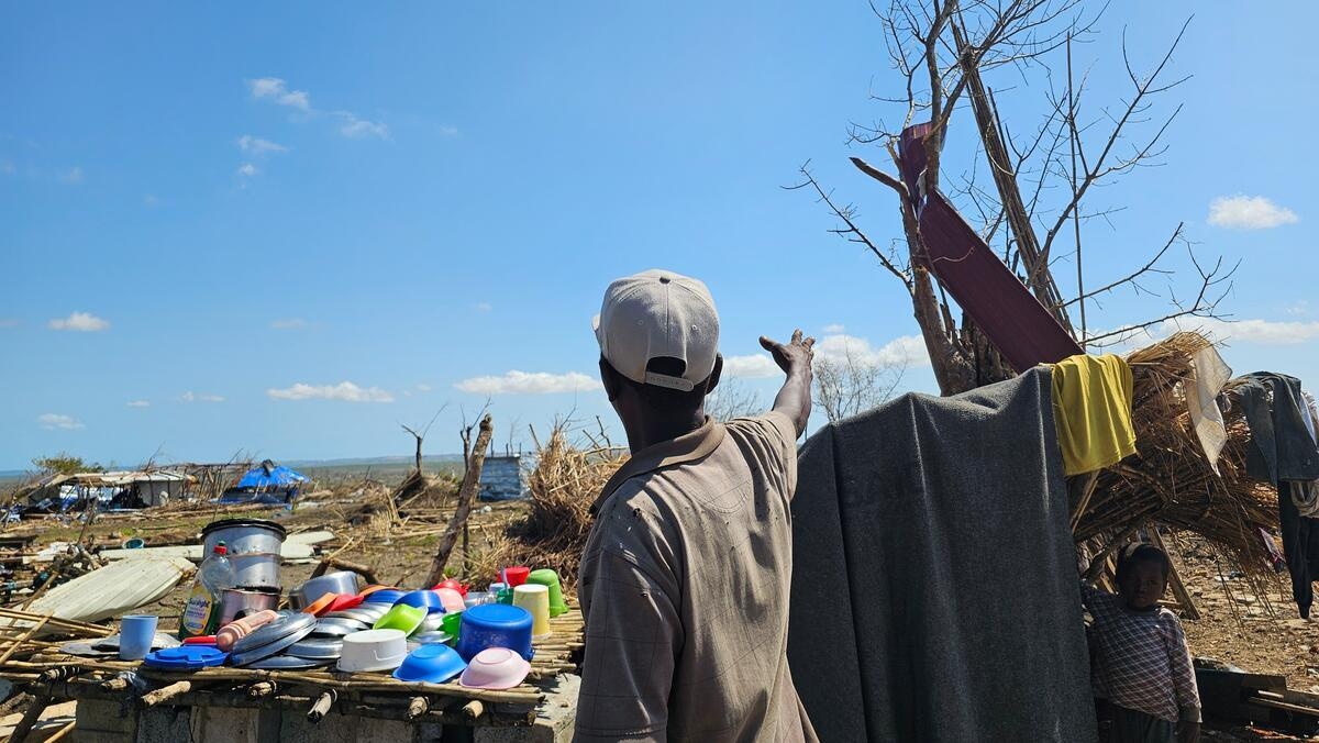 Un homme, dos à la caméra, fait un geste pour montrer un paysage endommagé par un cyclone.