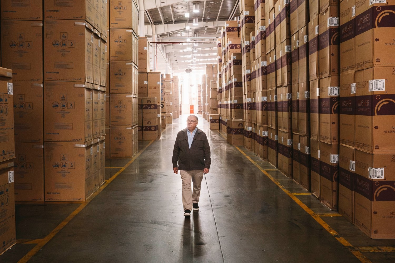 A man walks between towering stacks of cardboard boxes in a warehouse