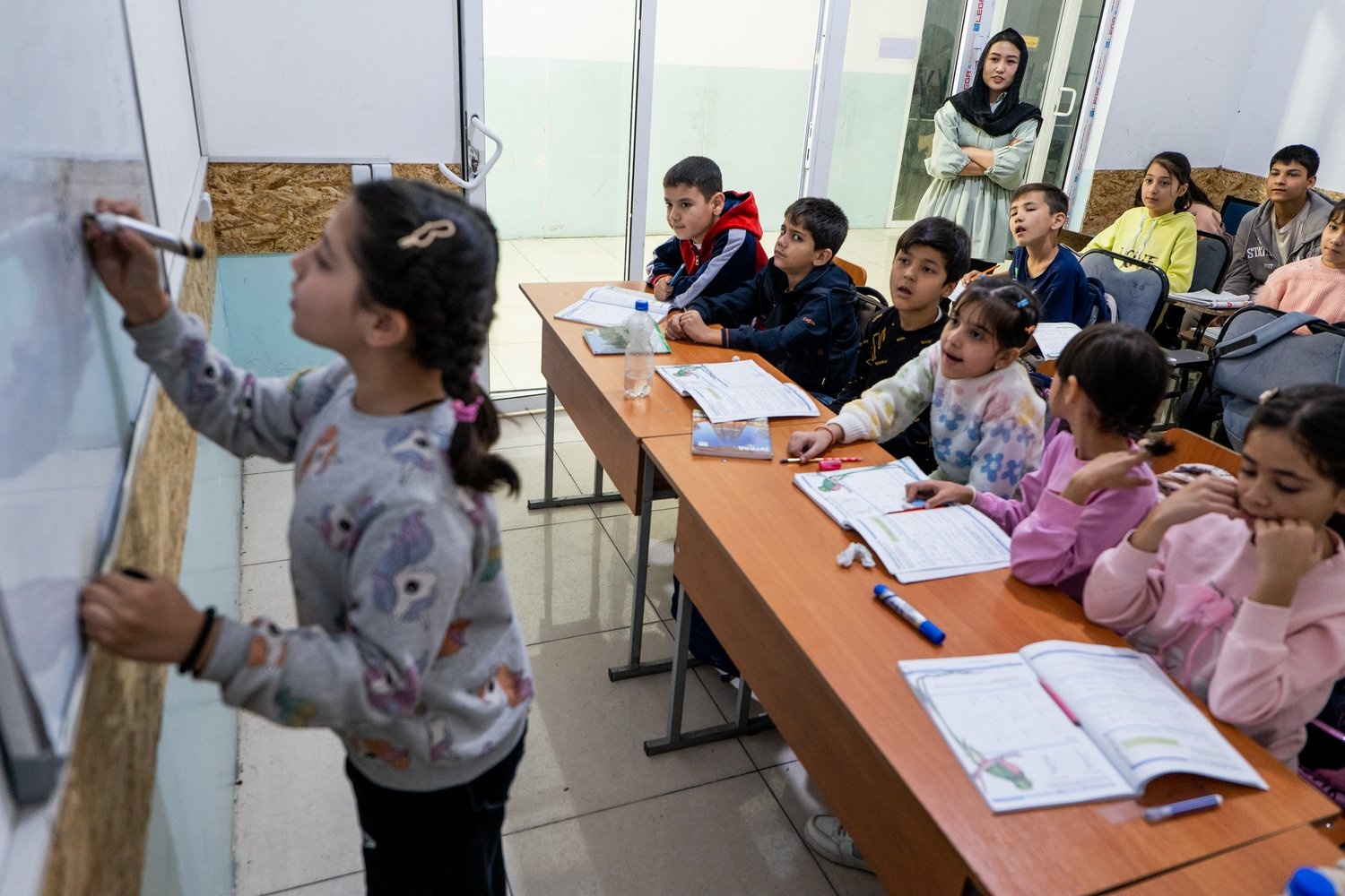 A girl writes on a whiteboard in front of a classroom of children