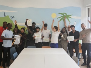 A group of young asylum seekers and staff smiling into the camera holding certificates from the art project.