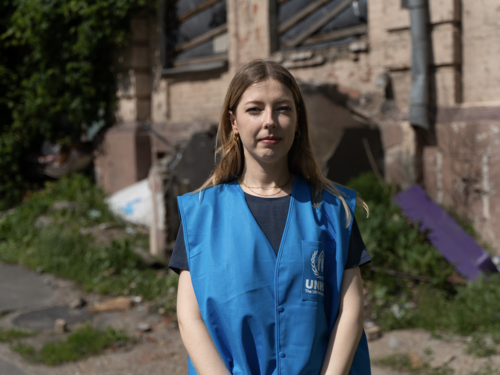 Eine UNHCR Mitarbeitende steht vor einem zerstörten Haus in der Ukraine