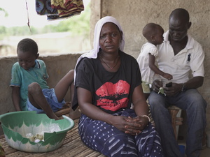 A woman sits staring into the camera while two small children and a man sit behind her. 