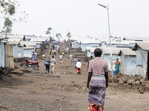 Des personnes marchent par un ou deux sur le sol sec et ondulé d'un camp des populations déplacées internes.