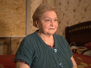 Une femme assise sur le bord d'un lit regarde au loin.