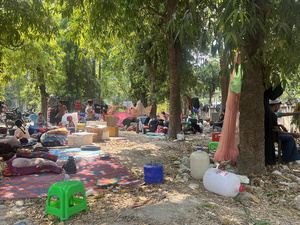 Families gather in the open under trees with their belongings.