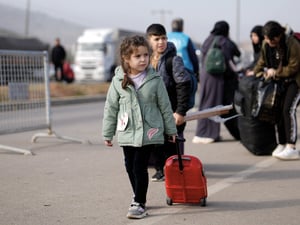 A young child walks on asphalt pulling a small suitcase.