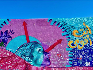 A wall painting in blue and pink shades picturing the head of a woman looking up towards the sky