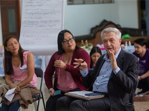 Two women and a man are talking while sitting in a room during a public event.
