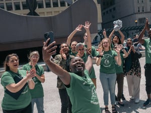 A group of smiling, cheering people take a selfie in Chicago at World Refugee Day celebrations