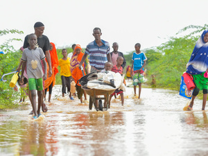 A man pushes a handcart containing a young child and his belongings through floodwaters accompanied by other family members.