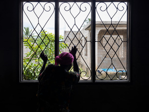 Une femme, dos à la caméra, regarde par la fenêtre, les mains posées sur les barres de sécurité.