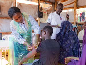 Several people receive vaccinations and other medical consultation in a makeshift shelter outdoors
