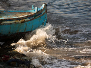 Waves crash against the bow of a teal fishing boat 