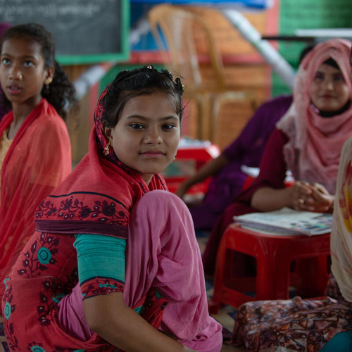 A group of girls wearing colorful clothing sit in a classroom.