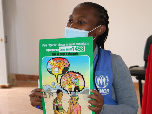 UNHCR personnel wearing a face mask holding up training resources in Spanish