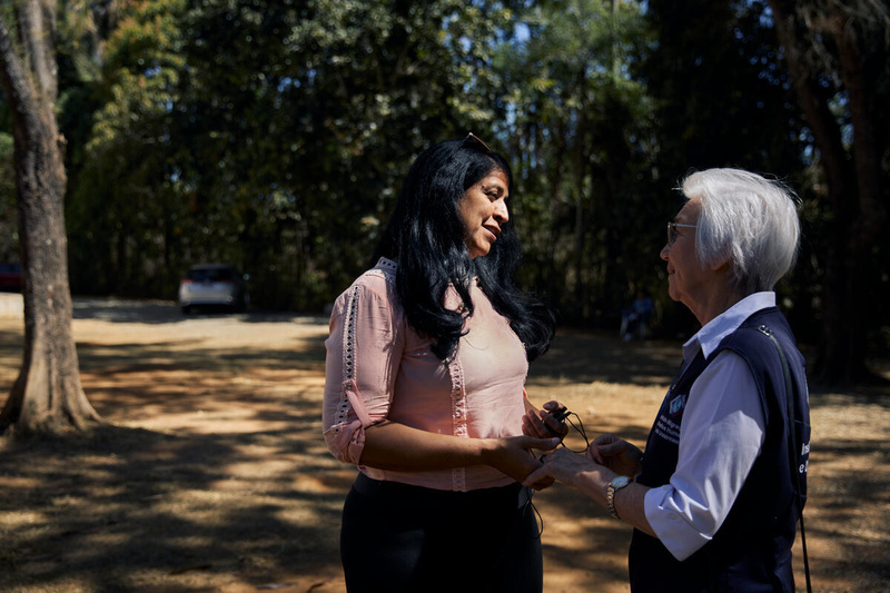 Two women hold hands as they talk outside in a shady garden