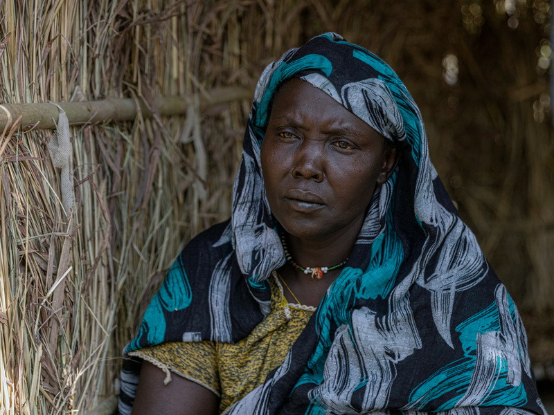 A woman in front of a thatched shelter.