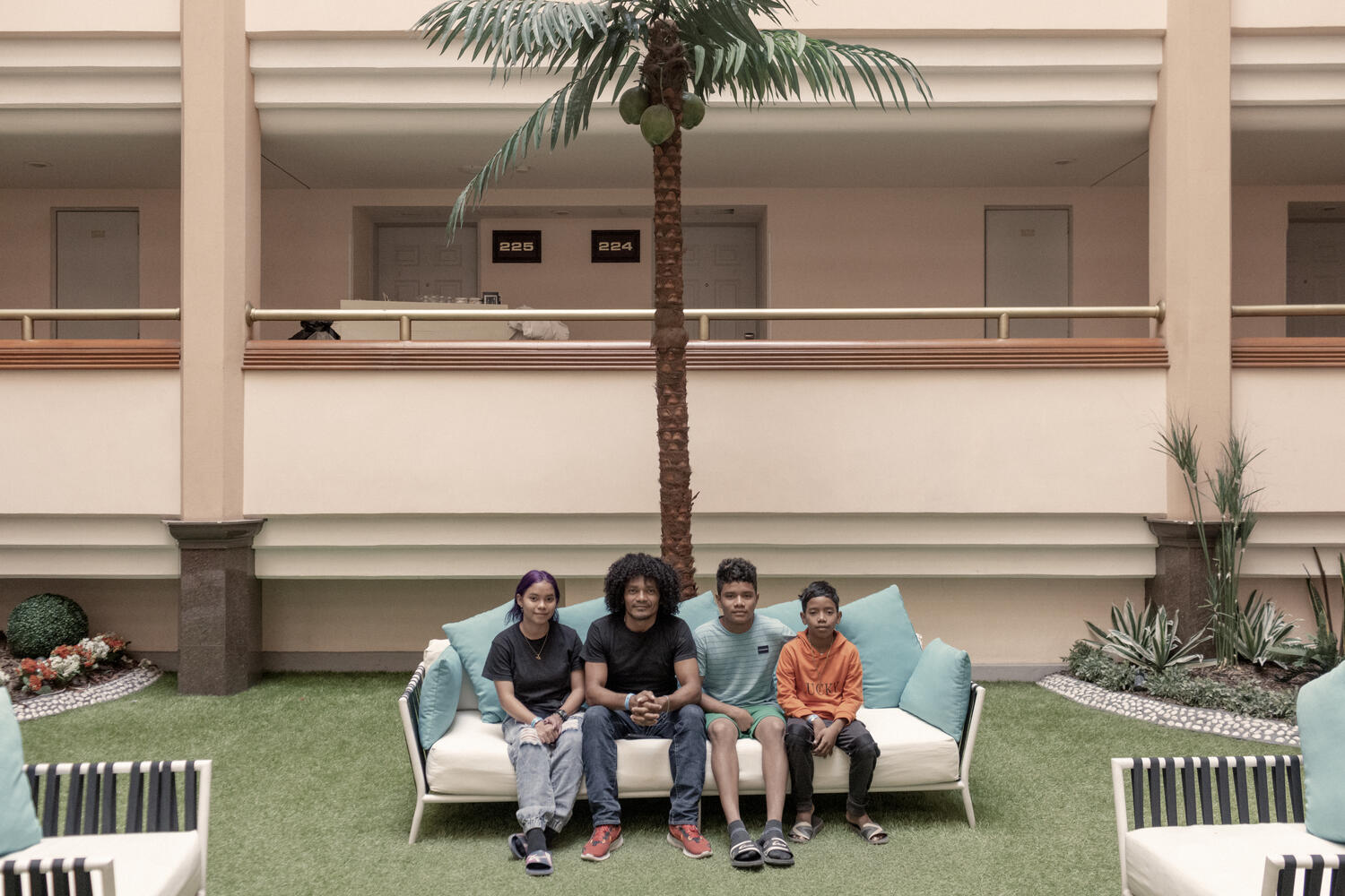 A man sits on a couch in a hotel with his three children. 