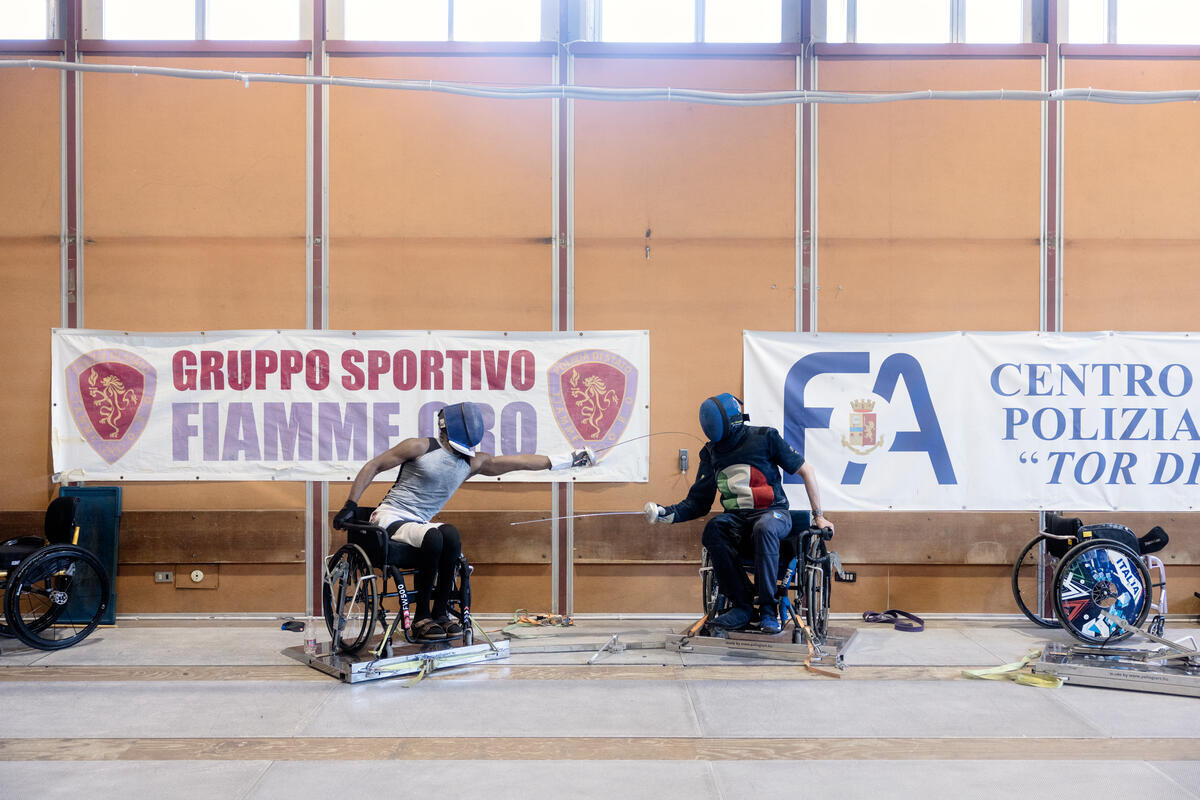 Two men in wheelchairs practice fencing.