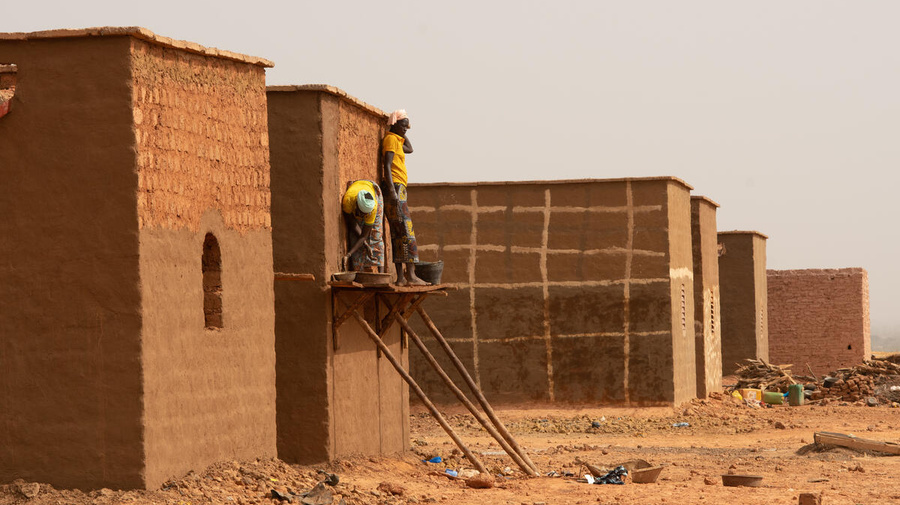 Two people apply mud stucco to the walls of a house under construction in Burkina Faso.