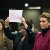 Three individuals stand together, one holds up a sign that reads 'I pledge'.