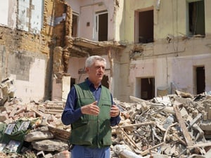 A man stands in front of the ruins of a heavily damaged building.