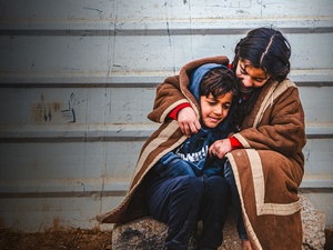 A young Syrian refugee wraps herself and her younger brother in a blanket as they sit outside in the cold in the Zaatari refugee camp.
