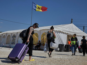 People carrying bags and pulling suitcases walk towards a large tent with a Moldovan flag flying above it